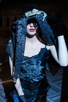 Artistic portrait of a woman wearing a lace veil and elegant dress in dim lighting.