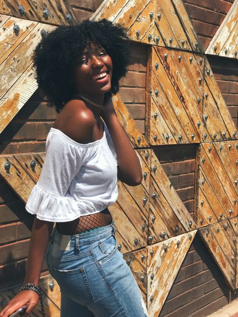 Beautiful black woman laughing outdoors, showcasing fashion and style against a textured wall.