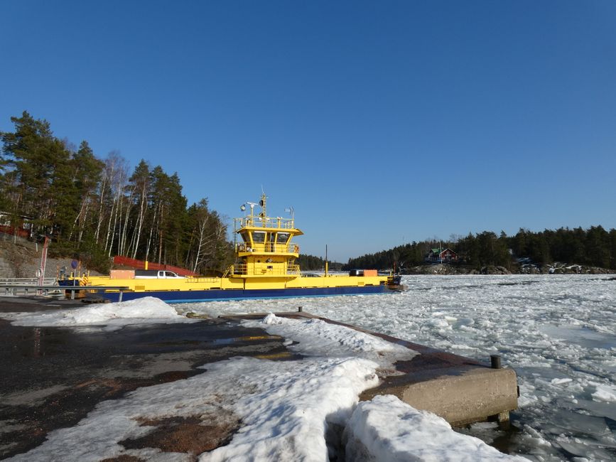 A vibrant yellow ferry navigating through a frozen harbor amidst a winter landscape under a clear blue sky.