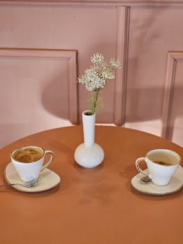 Stylish coffee setup on an orange table with white cups and a pink wall, creating a cozy ambiance.
