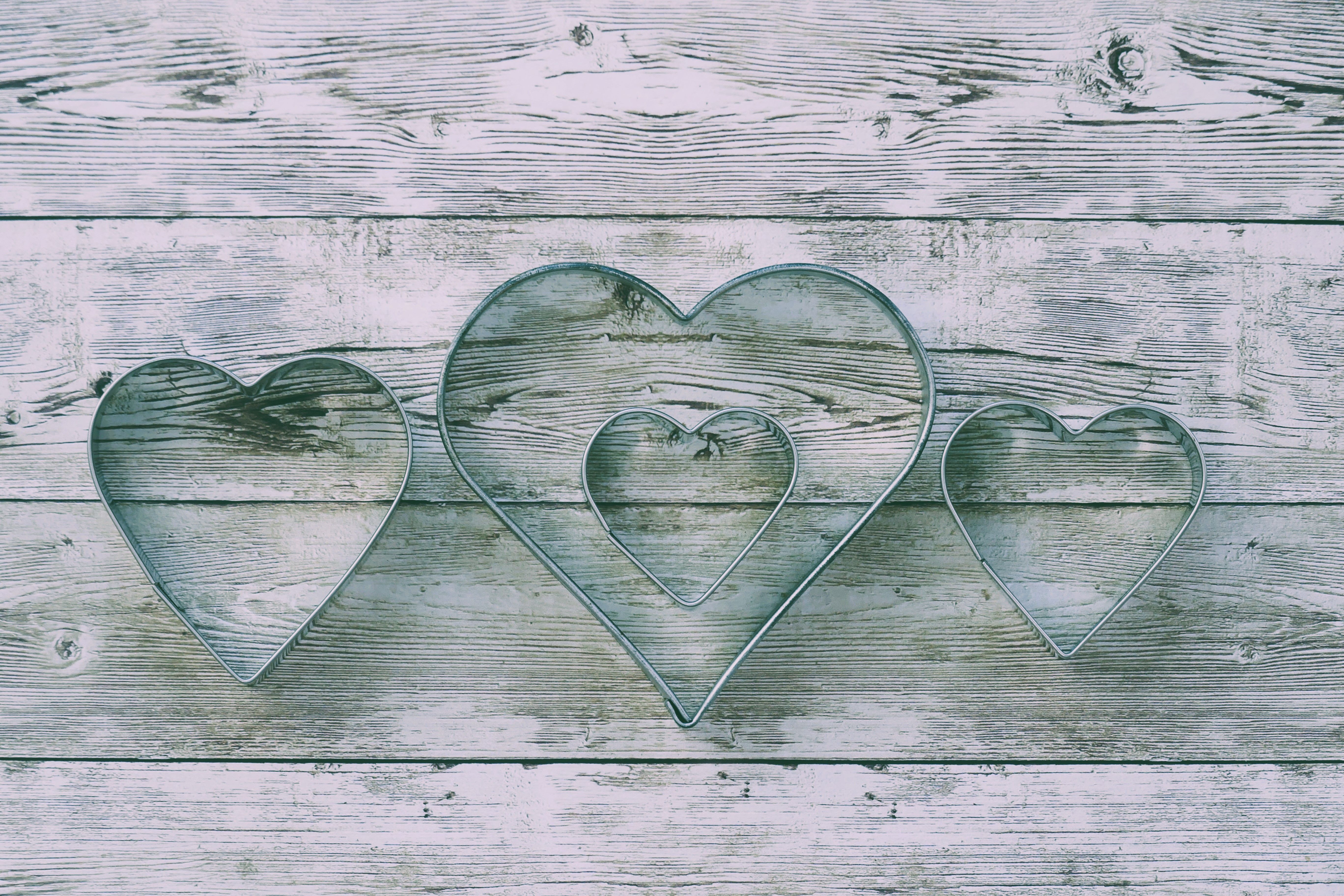 Three metal heart-shaped cookie cutters arranged on a rustic wooden background.