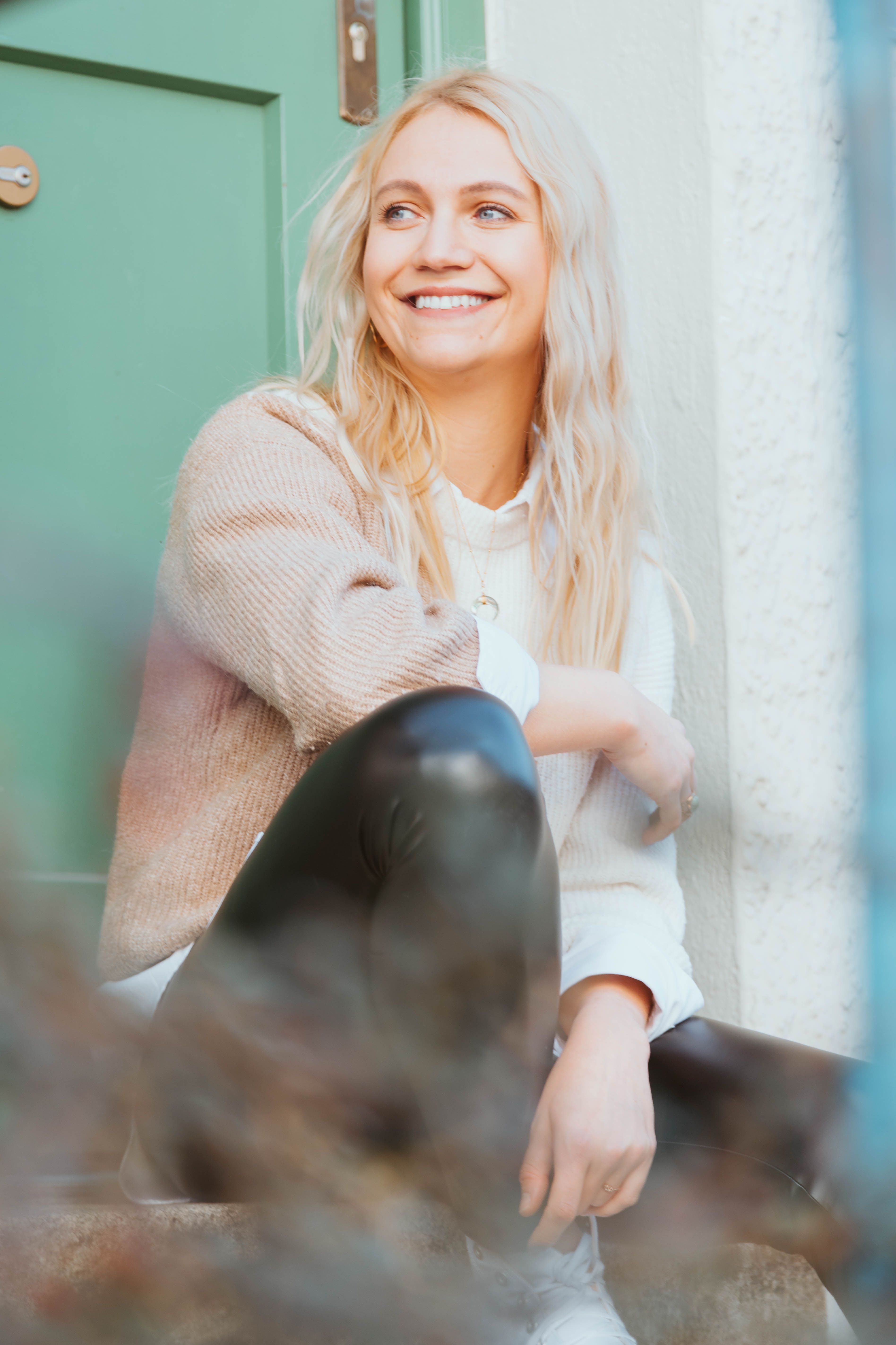 Happy young woman sitting outside a green door, smiling and relaxed.