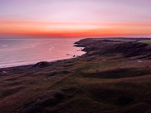 A sunset over the ocean with a grassy hill