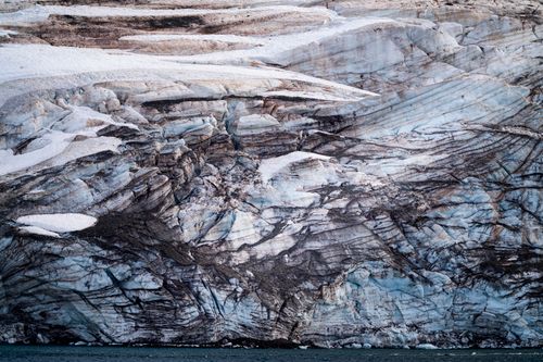 Free A stunning close-up of a glacier's textured ice and rock formations, showcasing natural beauty and geological patterns. Stock Photo