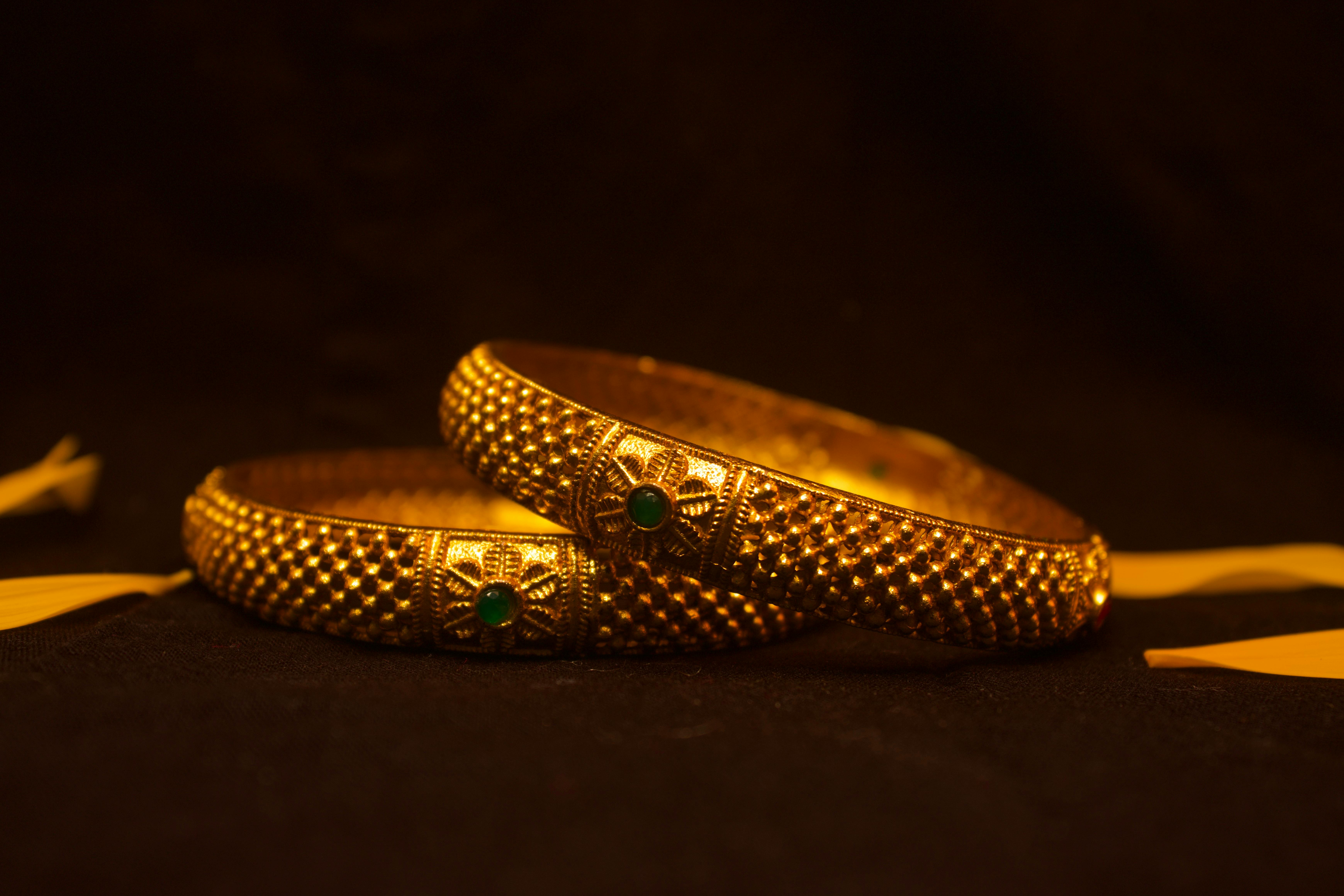 two gold bracelets on a black background