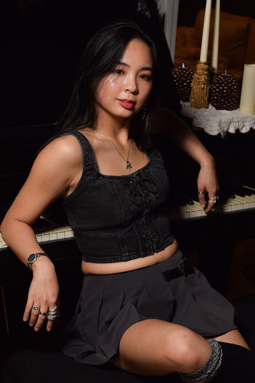 A woman in a skirt and top sitting on a piano