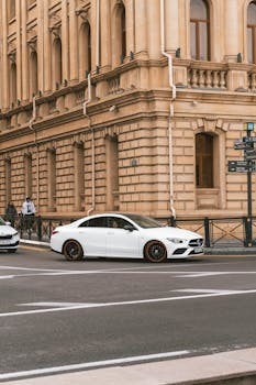 White luxury car parked by a historic building on a city street corner.