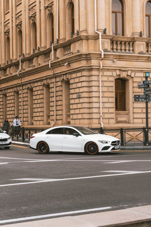 Free White luxury car parked by a historic building on a city street corner. Stock Photo