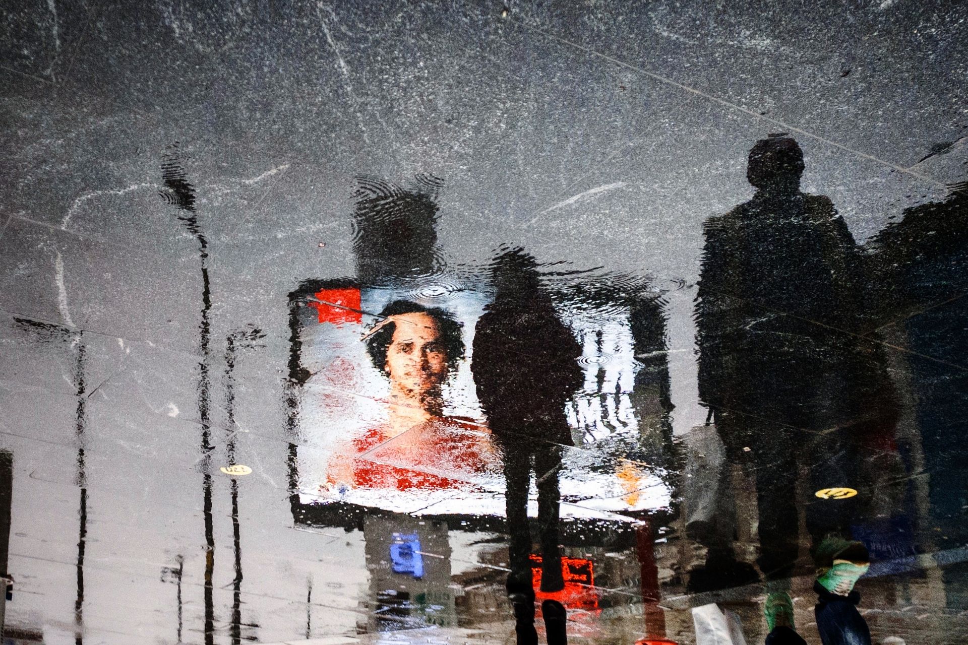 Reflection of people walking in İstanbul with a billboard on a rainy day.