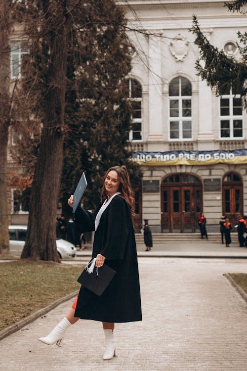 A woman in a black coat and white dress is standing outside a building
