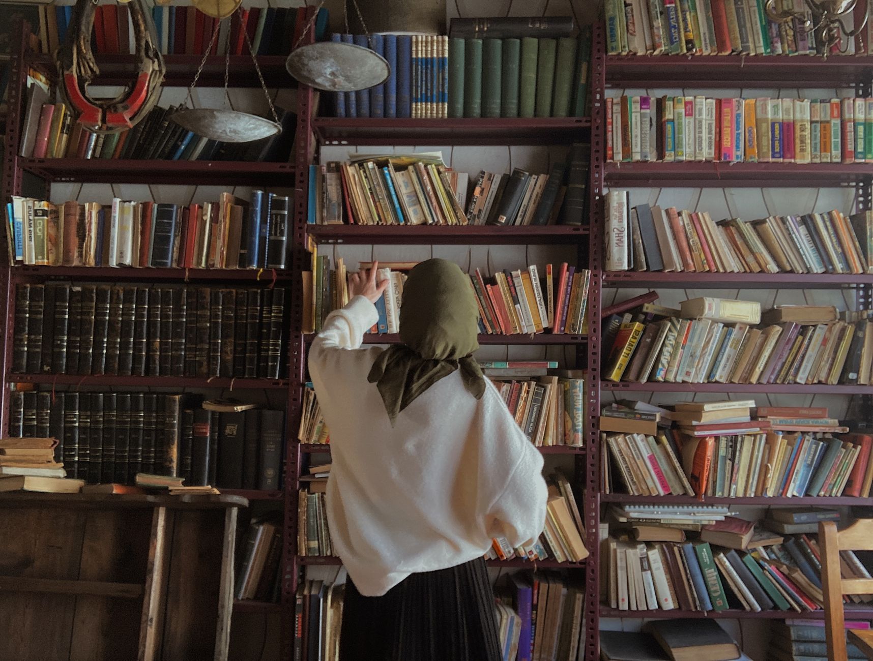 A woman wearing a headscarf explores a library filled with classic literature and bookshelves.