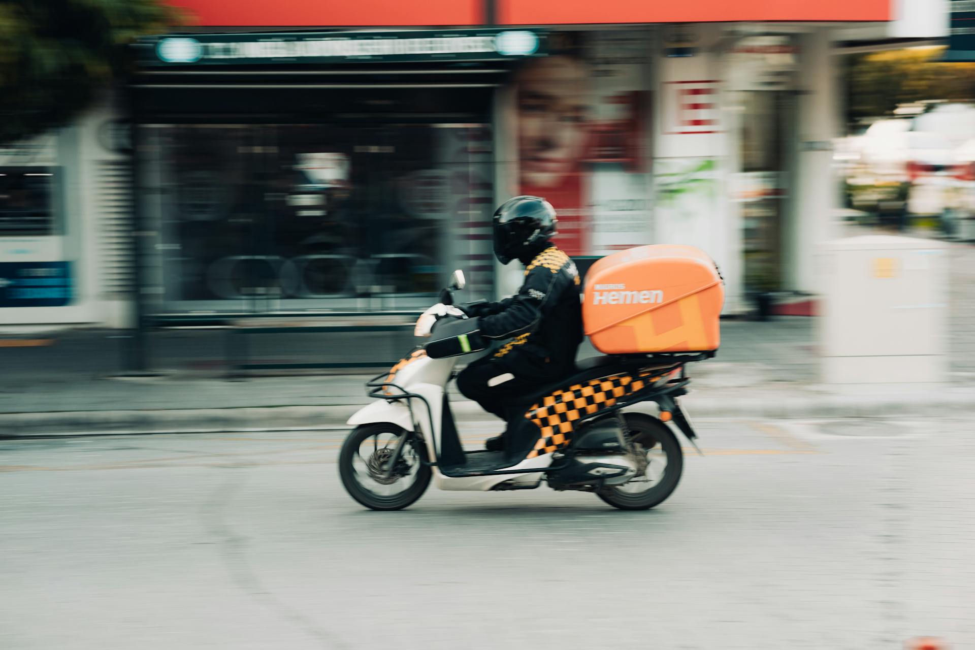 A delivery rider on a motor scooter speeds through city streets capturing urban transportation dynamics.