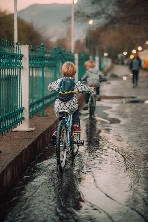 Back View of Children Riding Bicycles on a Street after Rain 
