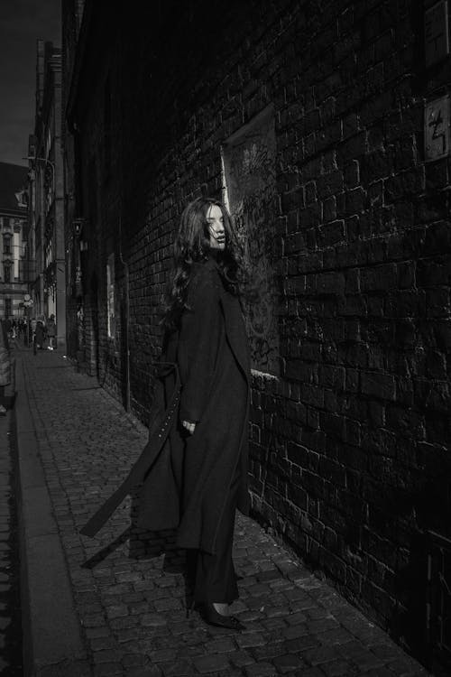 A woman in a long coat is walking down a dark alley