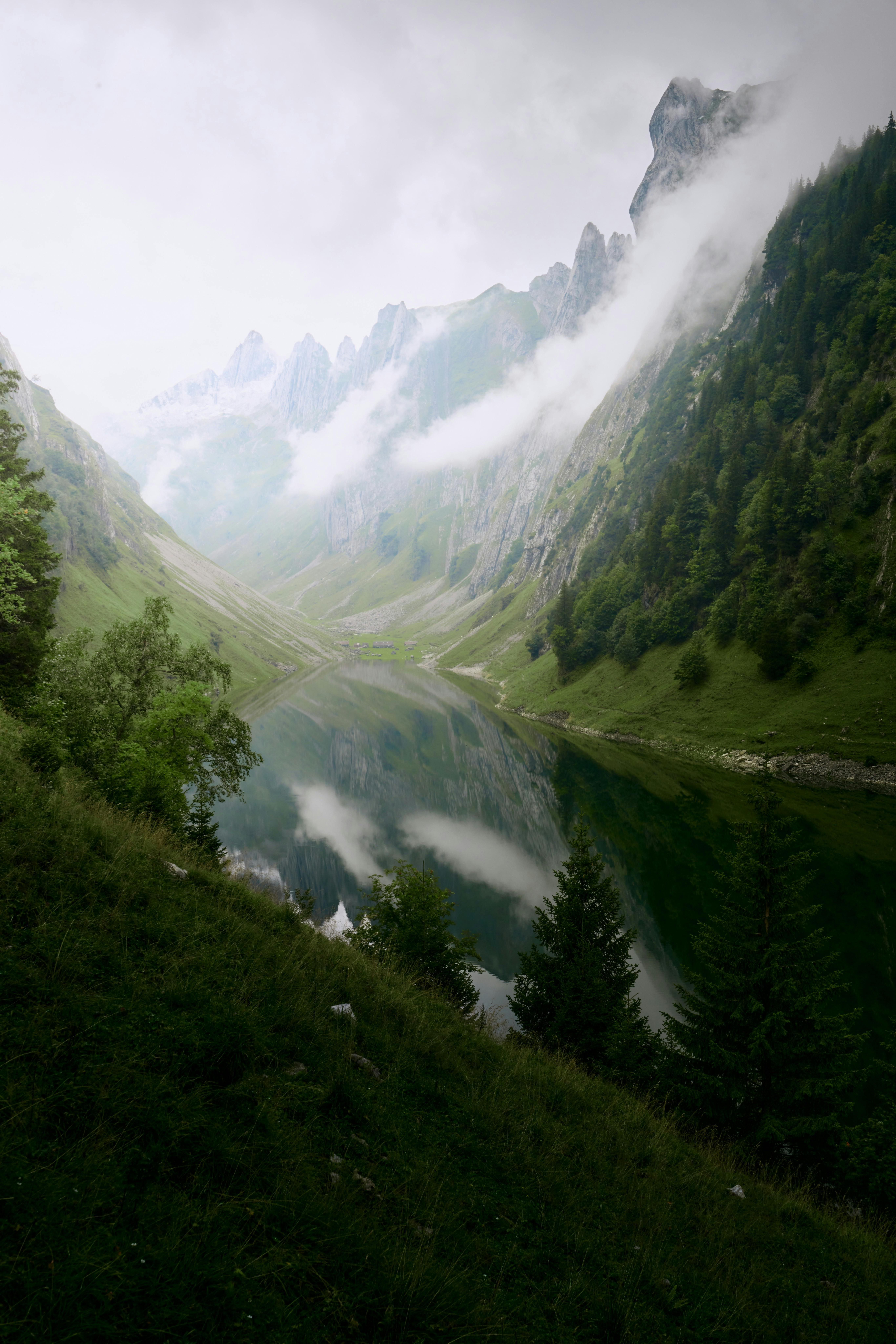 Tranquil Swiss valley landscape with misty mountains and reflective lake.