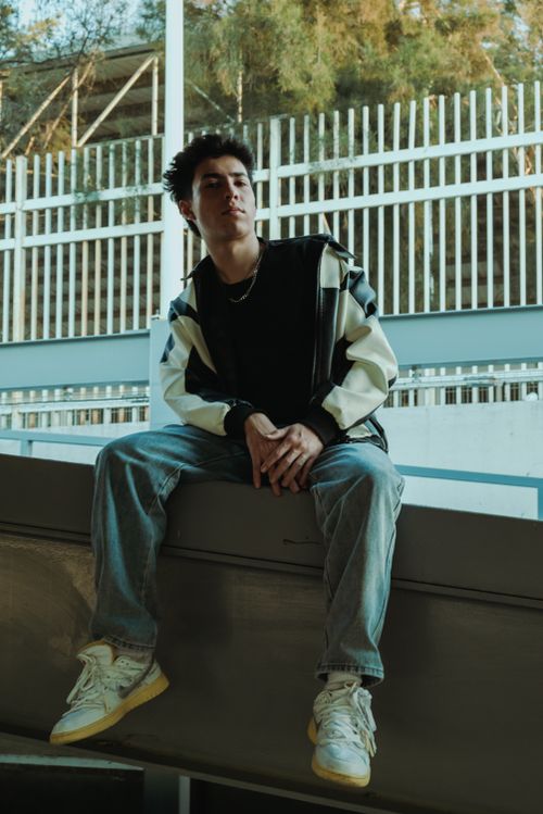 Free Stylish young man with short hair sitting against an urban backdrop wearing jeans and a jacket. Urban vibe. Stock Photo
