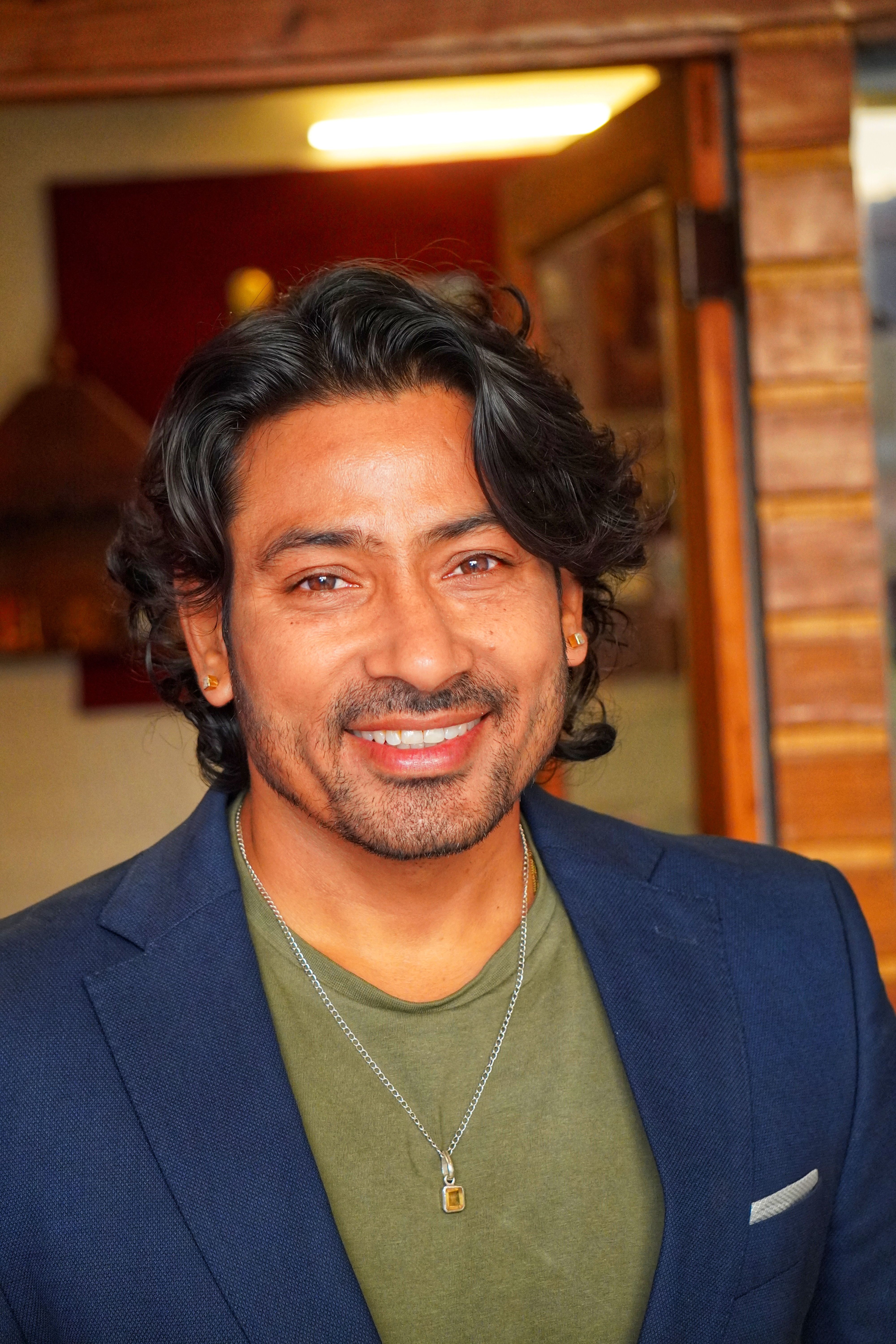 Portrait of a smiling man in a blue suit with wavy hair, indoors.