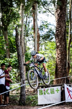 Dynamic shot of a mountain biker jumping midair during a forest race with spectators watching.