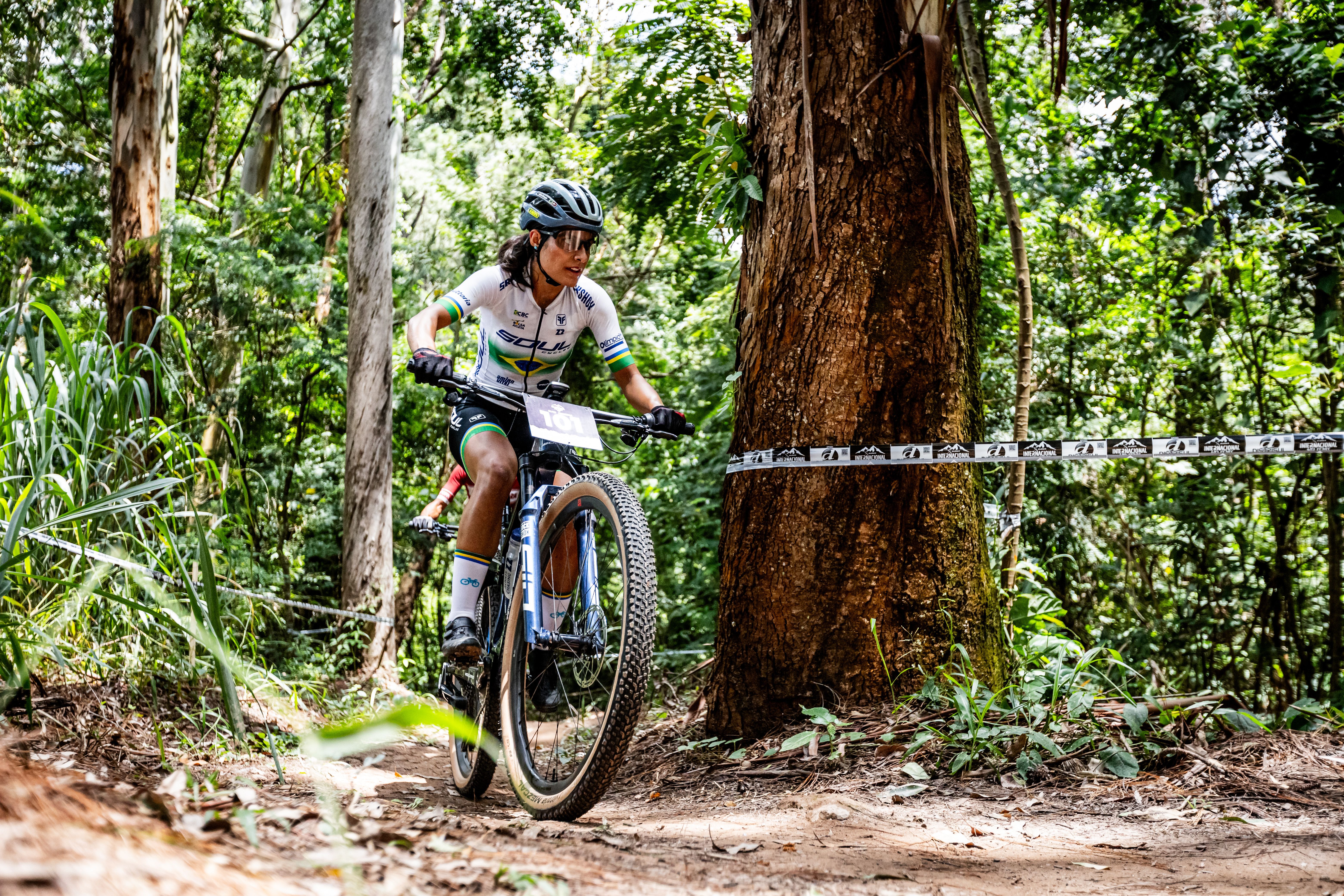Female cyclist on mountain bike racing through a forest trail on a sunny day.