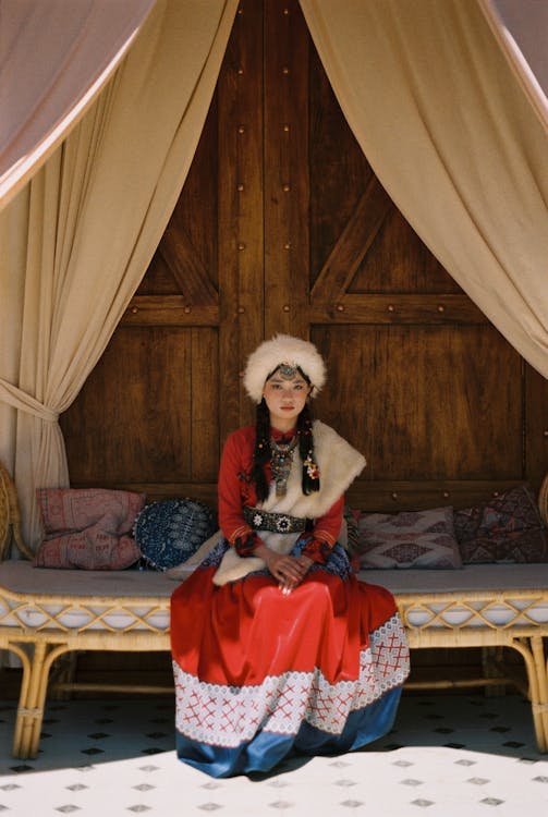 Young Woman in Folk Costume Sitting on a Sofa in a Yurt