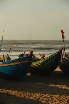 Vibrant fishing boats on a sandy beach with ocean waves in the background during sunset.