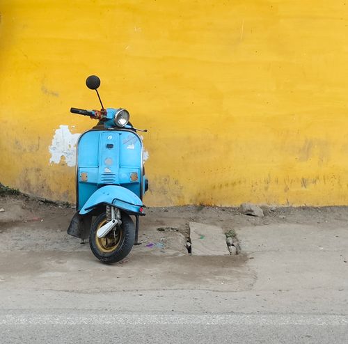 Free A vintage blue scooter parked against a vibrant yellow wall in Udaipur, India, showcasing colorful street life. Stock Photo