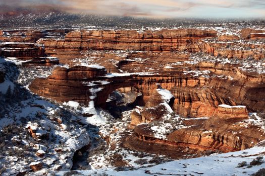 Breathtaking winter landscape of Canyonlands with snow-covered rock formations and arches under a clear sky.