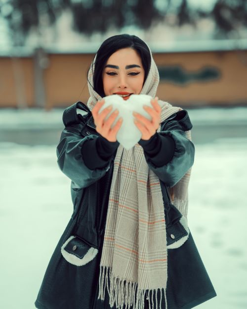Free A woman in a winter jacket and scarf holds a heart-shaped snow piece outdoors. Stock Photo