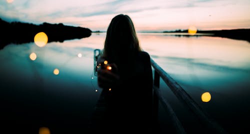 Silueta De Mujer Recostada Sobre Barandillas De Metal Con Fondo De Cuerpo De Agua Por La Costa