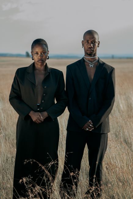 A stylish couple standing elegantly in a rural field, showcasing fashion.