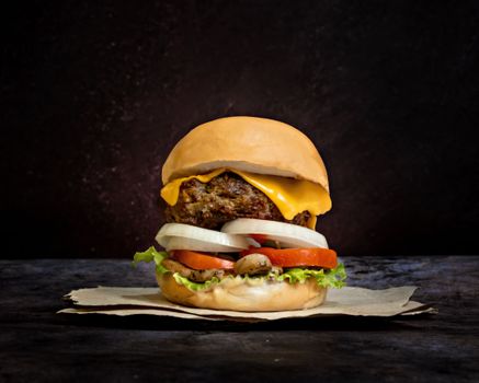 Mouth-watering burger with cheese, tomato, and lettuce on dark background.
