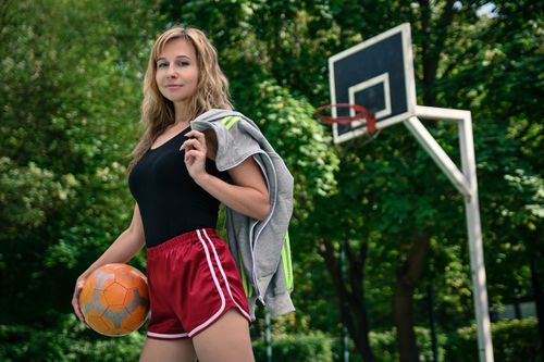 Free Athletic woman holding a ball while standing on an outdoor basketball court with a smile. Stock Photo