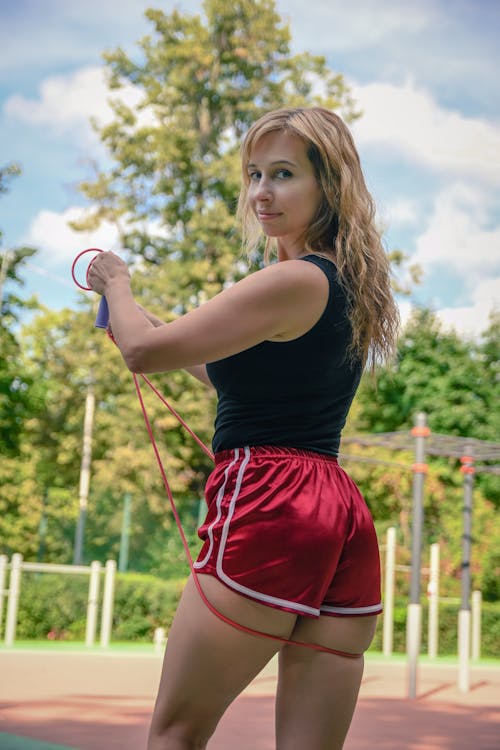 A woman in shorts and a red top is holding a tennis racket