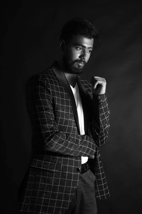 Free Black and white portrait of a man in a checkered blazer, deep in thought, set against a dark background. Stock Photo