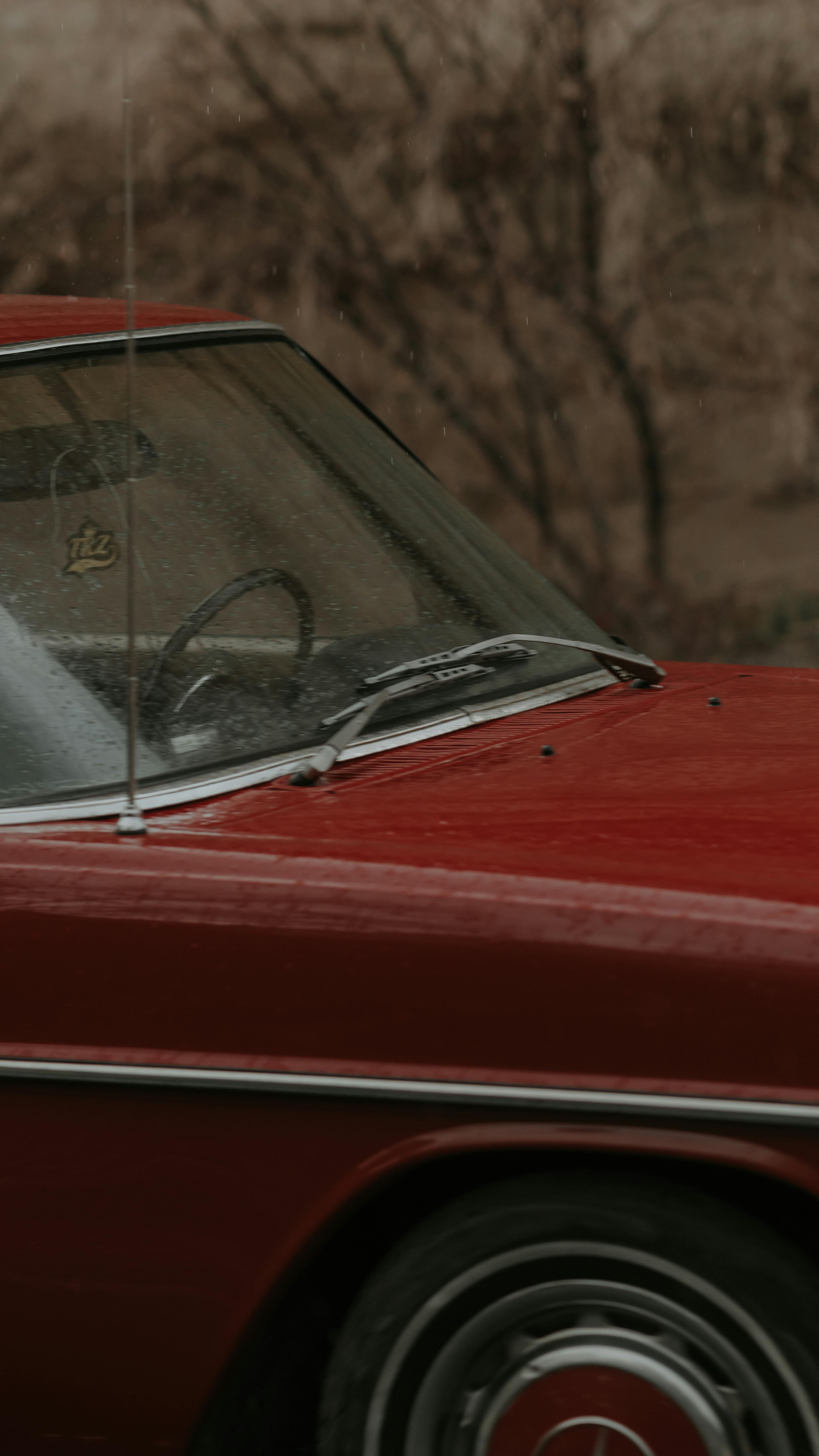 Classic red Mercedes-Benz with rain-soaked windows and wet exterior on a gloomy day.