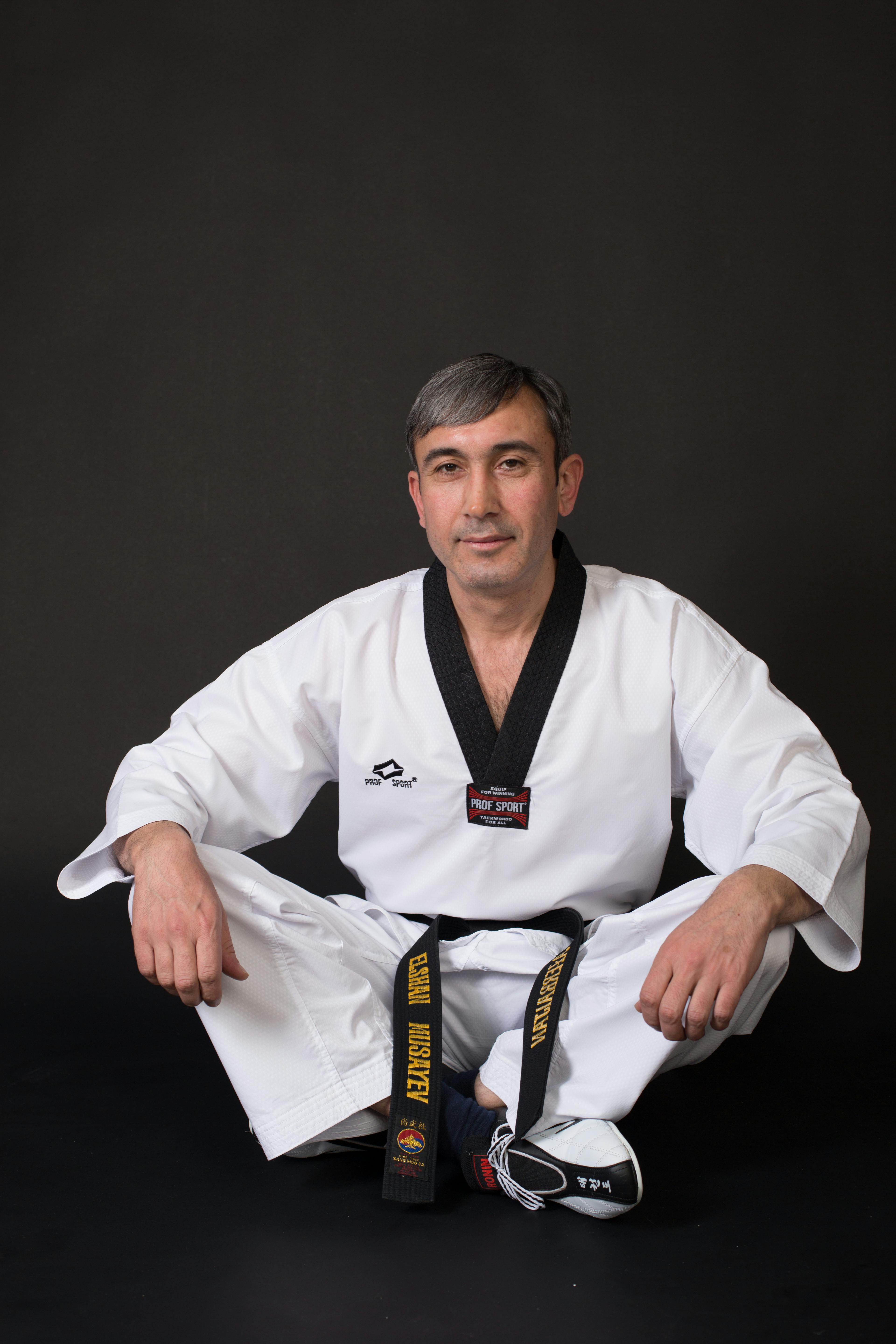 Portrait of a martial artist in traditional attire sitting cross-legged in a studio setting.