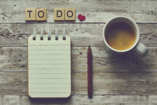 Flat lay of a notebook, pencil, coffee cup, and 'To Do' tiles on a rustic wooden table.