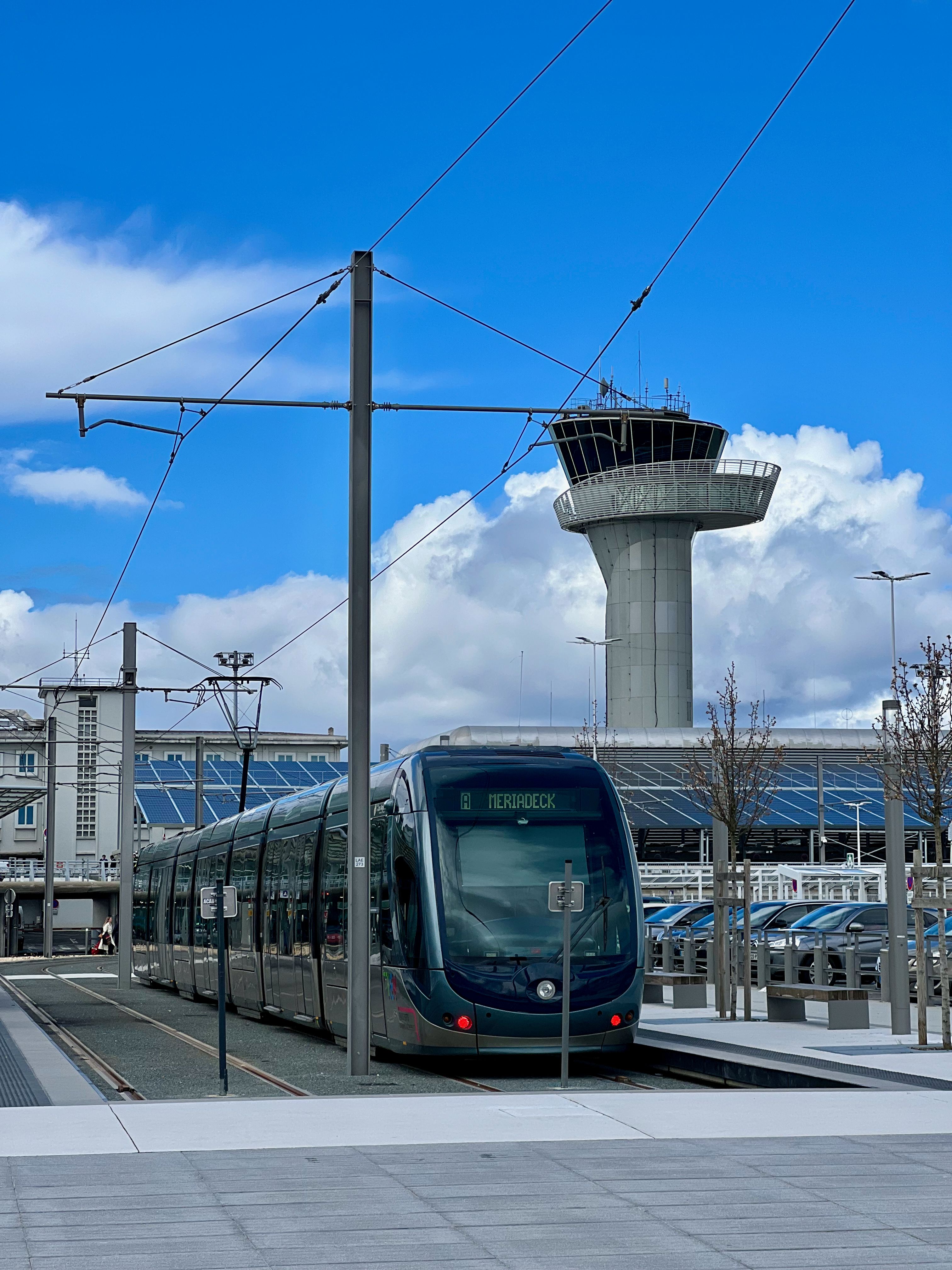 A sleek tram at Bordeaux Airport with control tower in the background.
