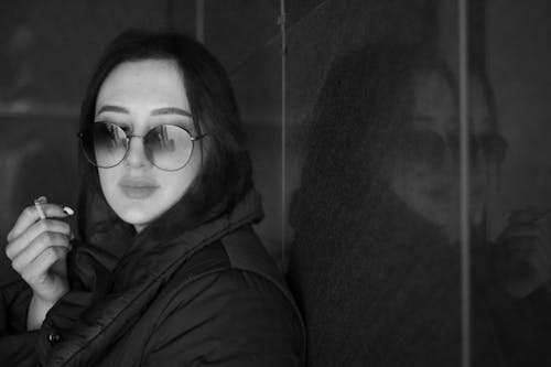 A woman in sunglasses and a jacket leaning against a wall