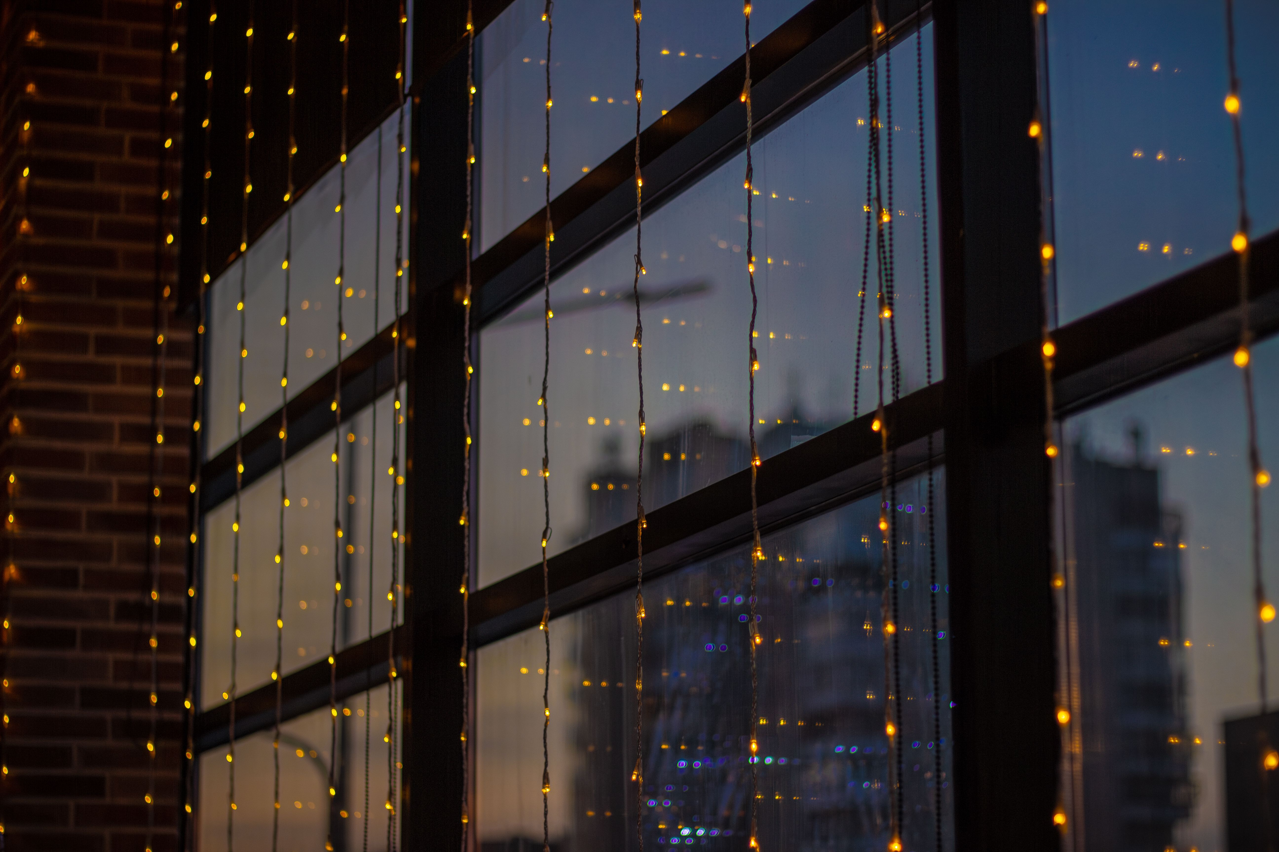 Soft twilight reflection of cityscape through window adorned with fairy lights.