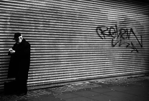 A man in a coat standing next to a wall with graffiti