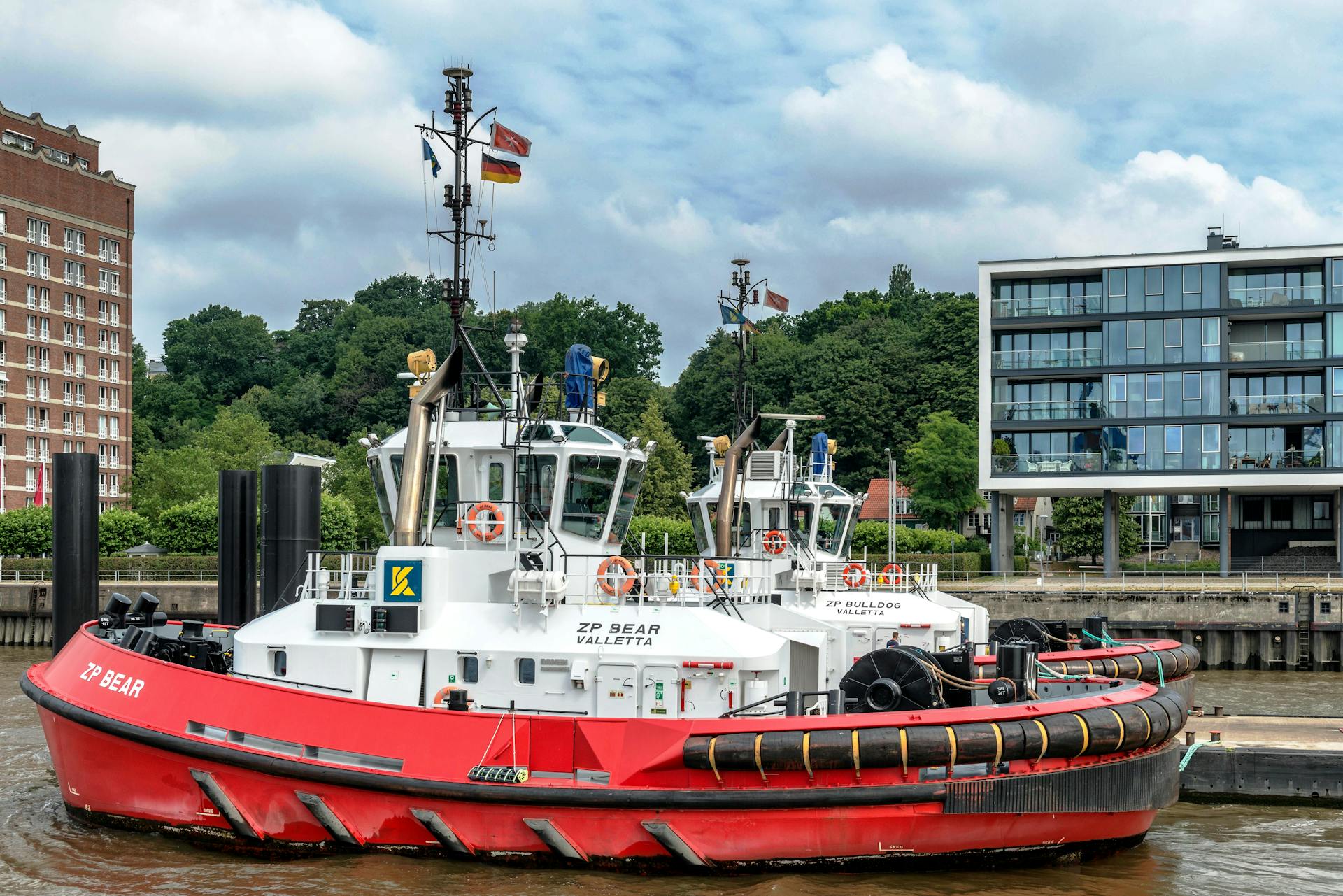 Red tugboat ZP Bear navigating Hamburg's urban harbor with modern architecture backdrop.