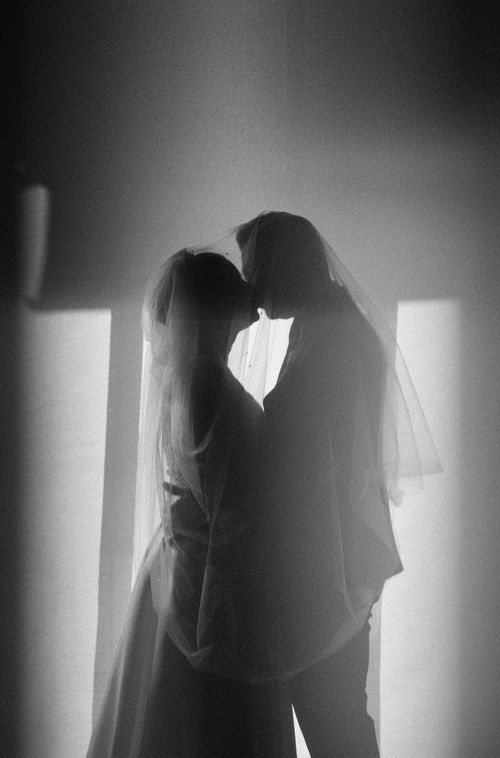 Free Artistic black and white photo of a newlywed couple kissing, shrouded in soft light. Stock Photo