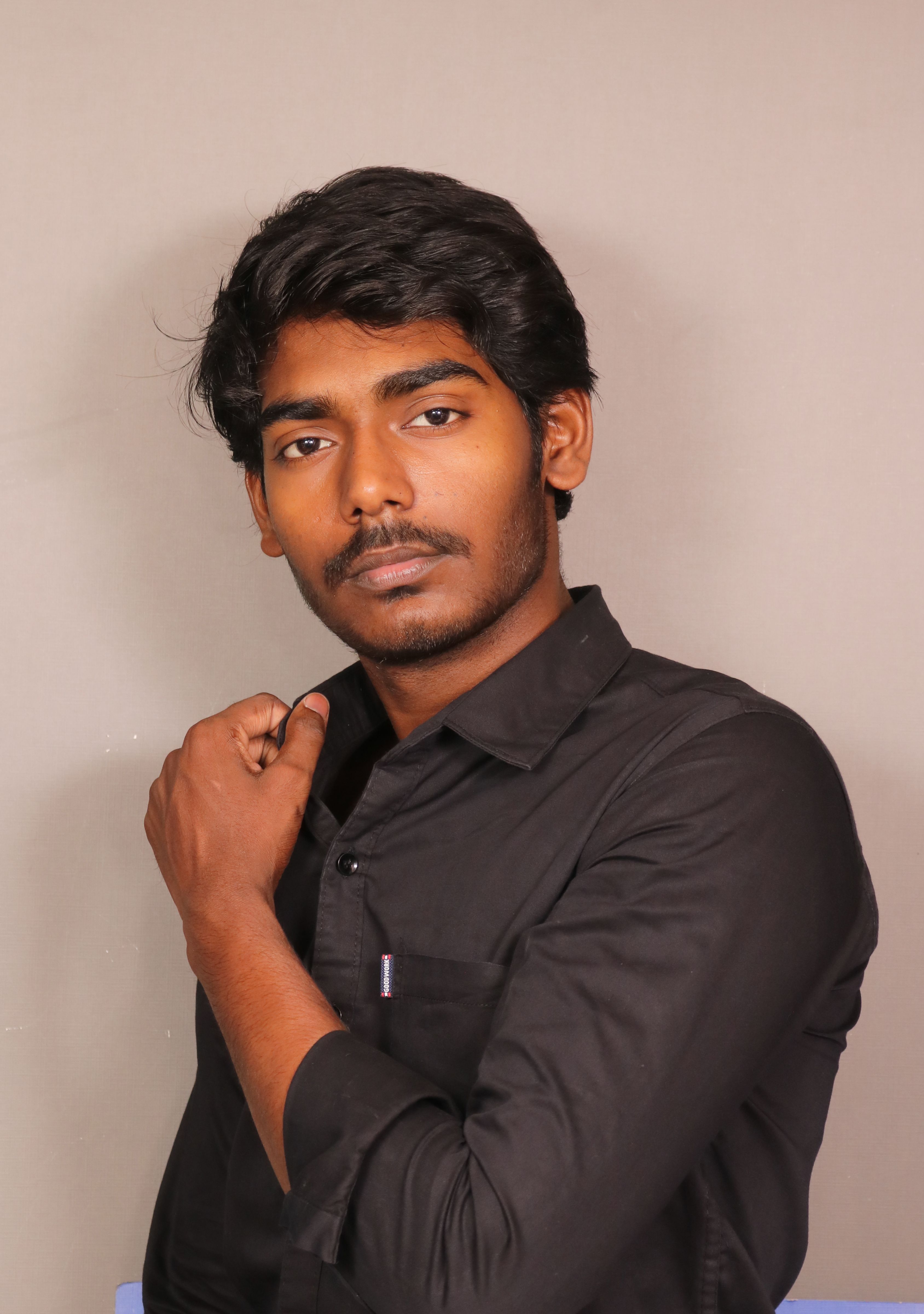 Studio portrait of a young South Asian man wearing a black shirt.