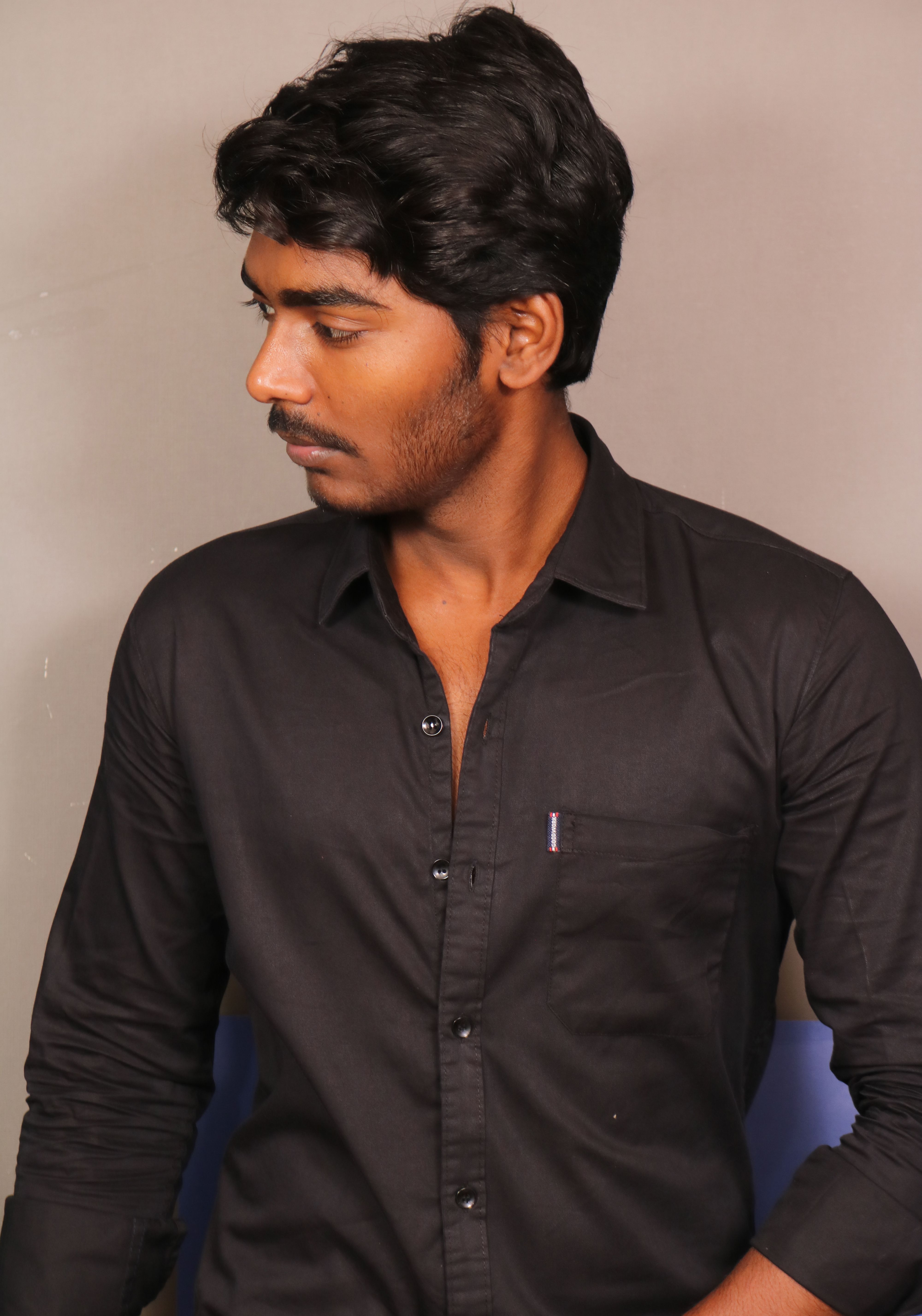 Portrait of a man in a black shirt looking away, showing poise and style.