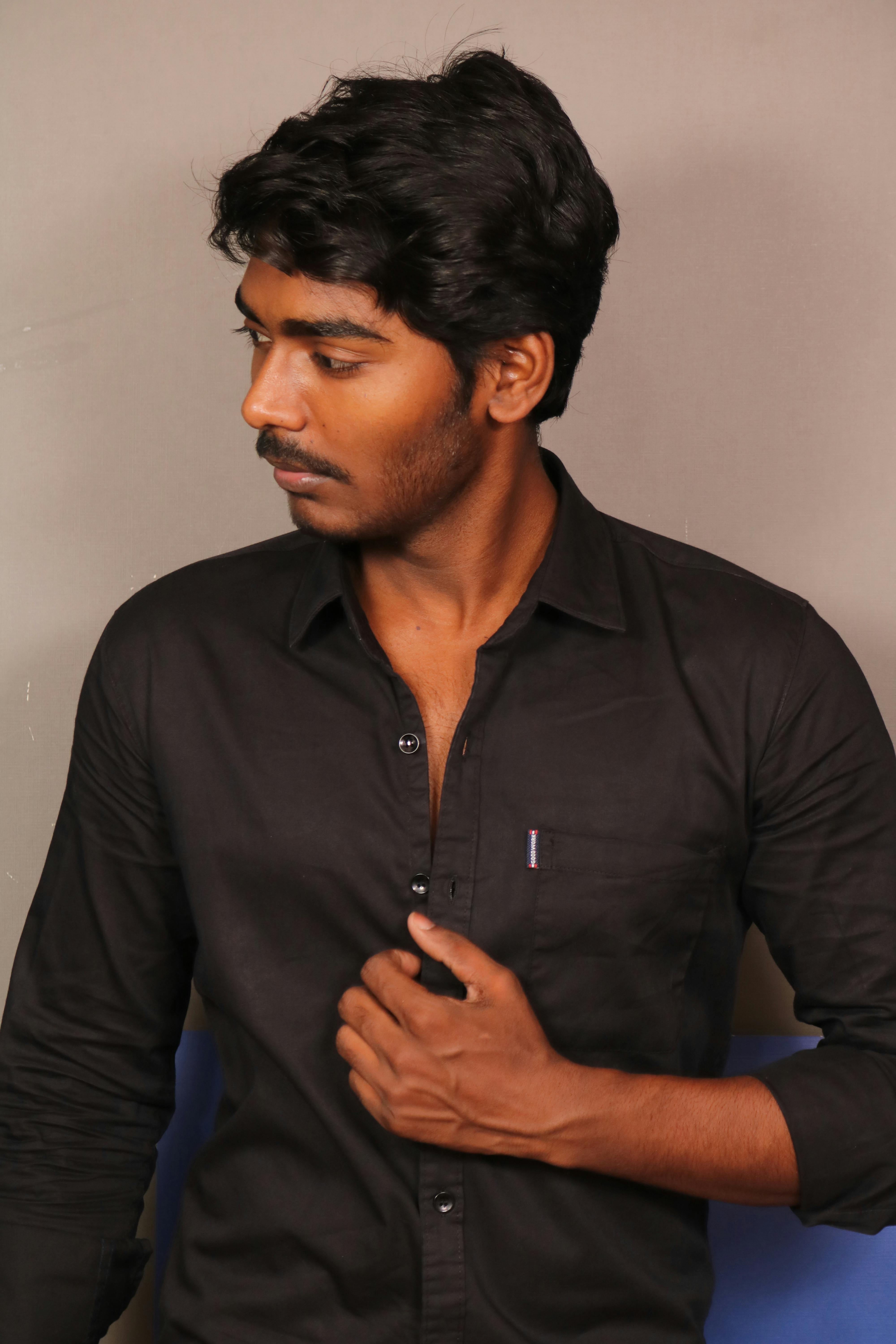 Elegant portrait of a South Asian man in black shirt with thoughtful expression indoors.