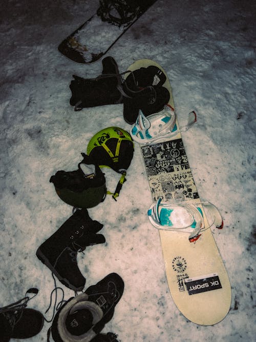 A snowboard, snow boots, and other items are laying on the ground