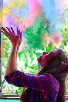 A woman joyfully throws vibrant powder into the air during Holi festival, celebrating with energy and color.