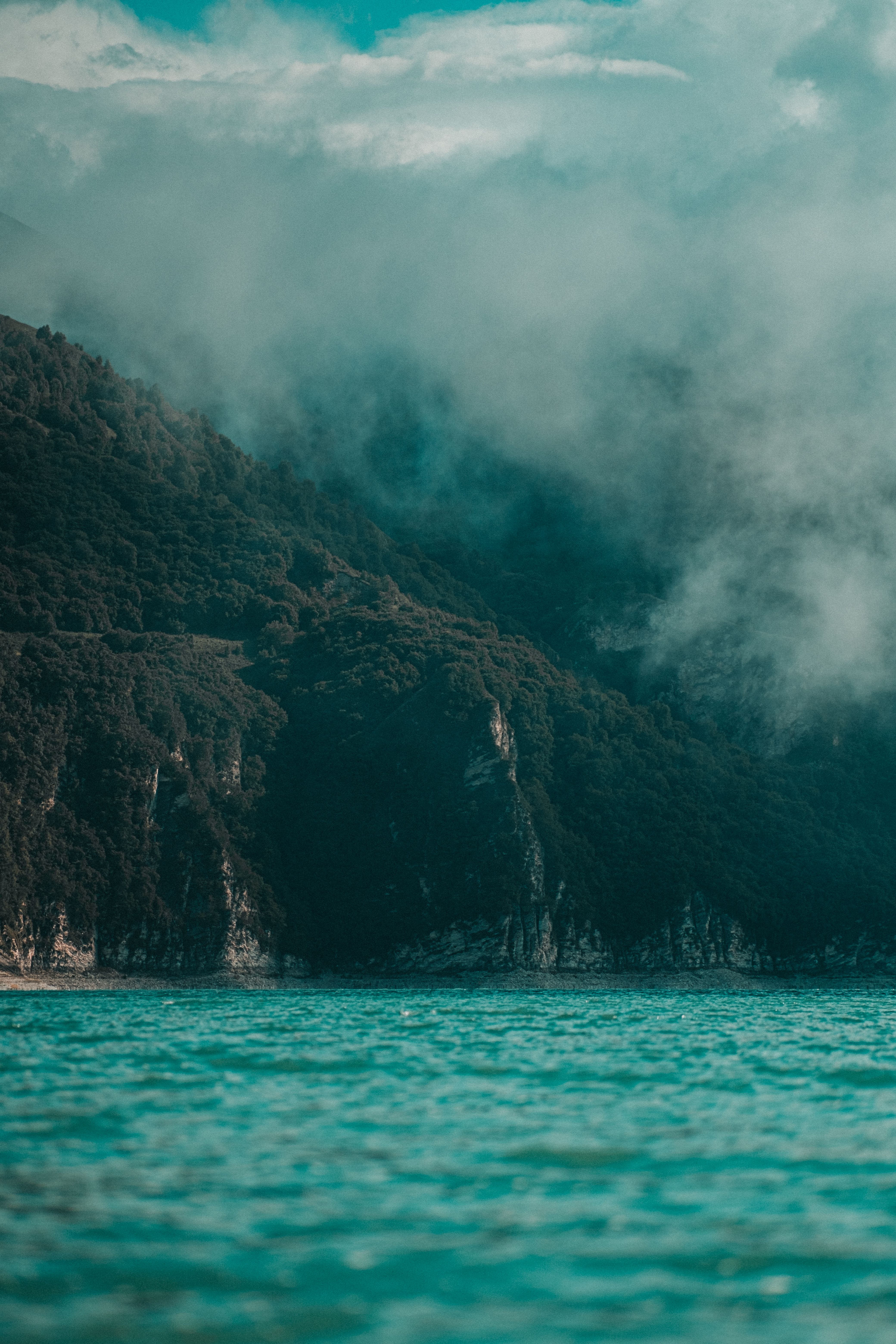 Mist over a forested ridge above teal water — photo by Zaur Takhgiriev on Pexels