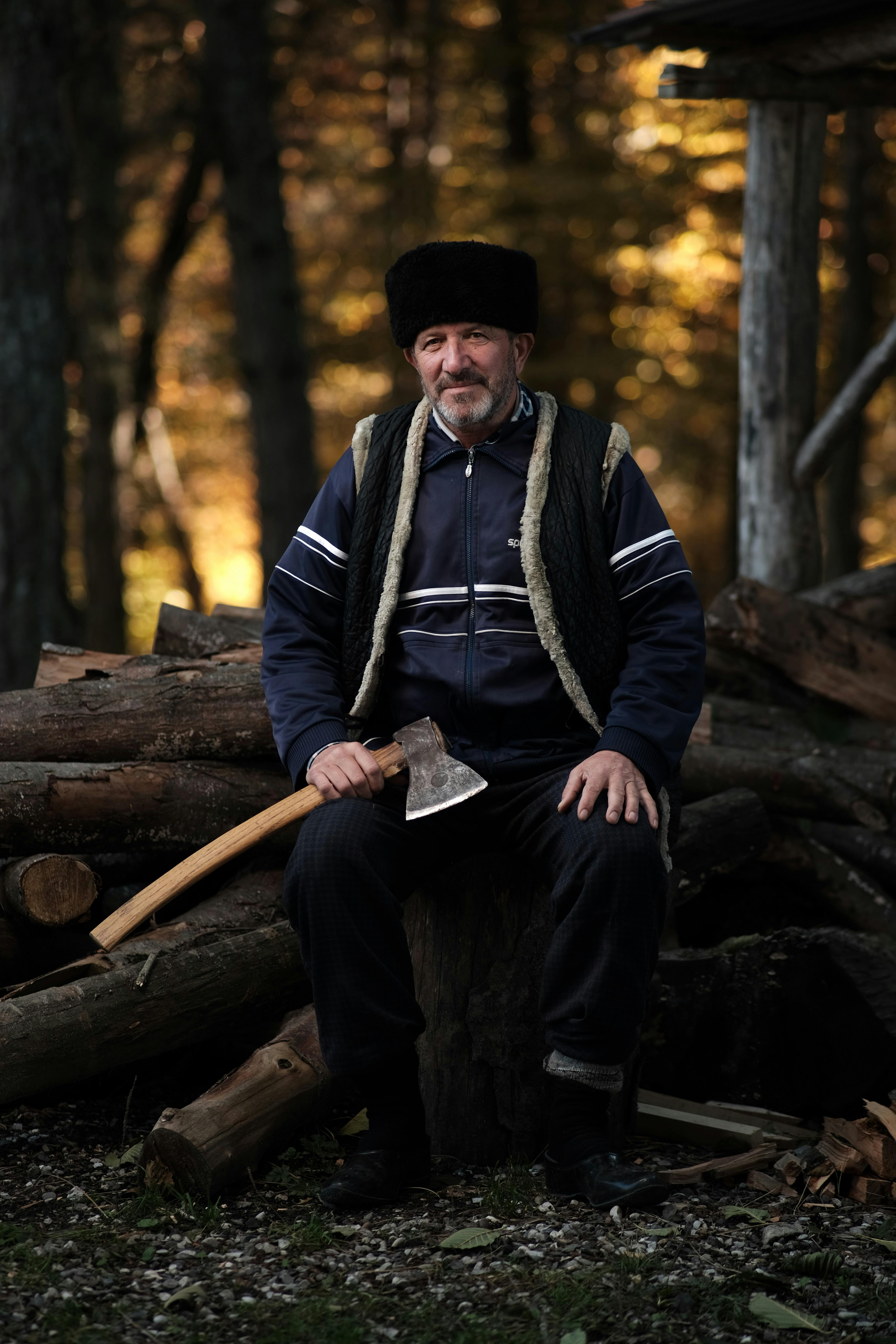 A lumberjack with an axe sits on logs in a serene forest location, surrounded by nature.